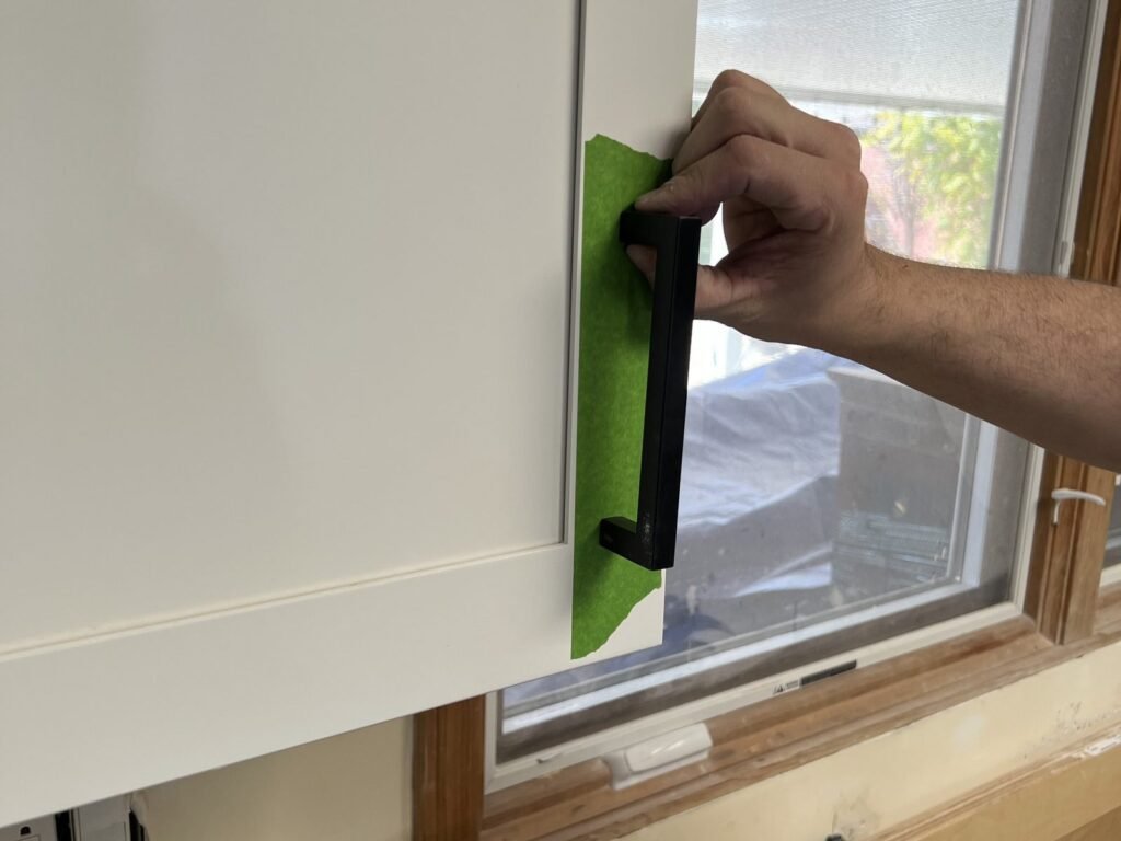 Black bar handle being fitted to a white shaker cabinet door