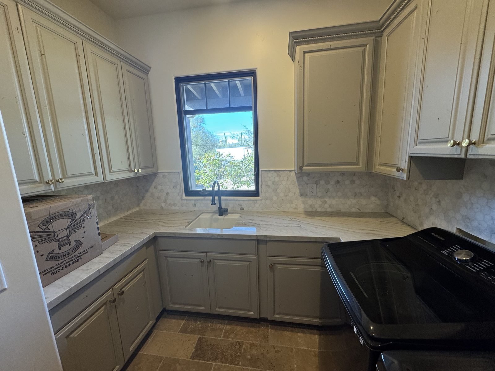 The same laundry cabinets repainted cream and grey with a new countertop and tile backsplash