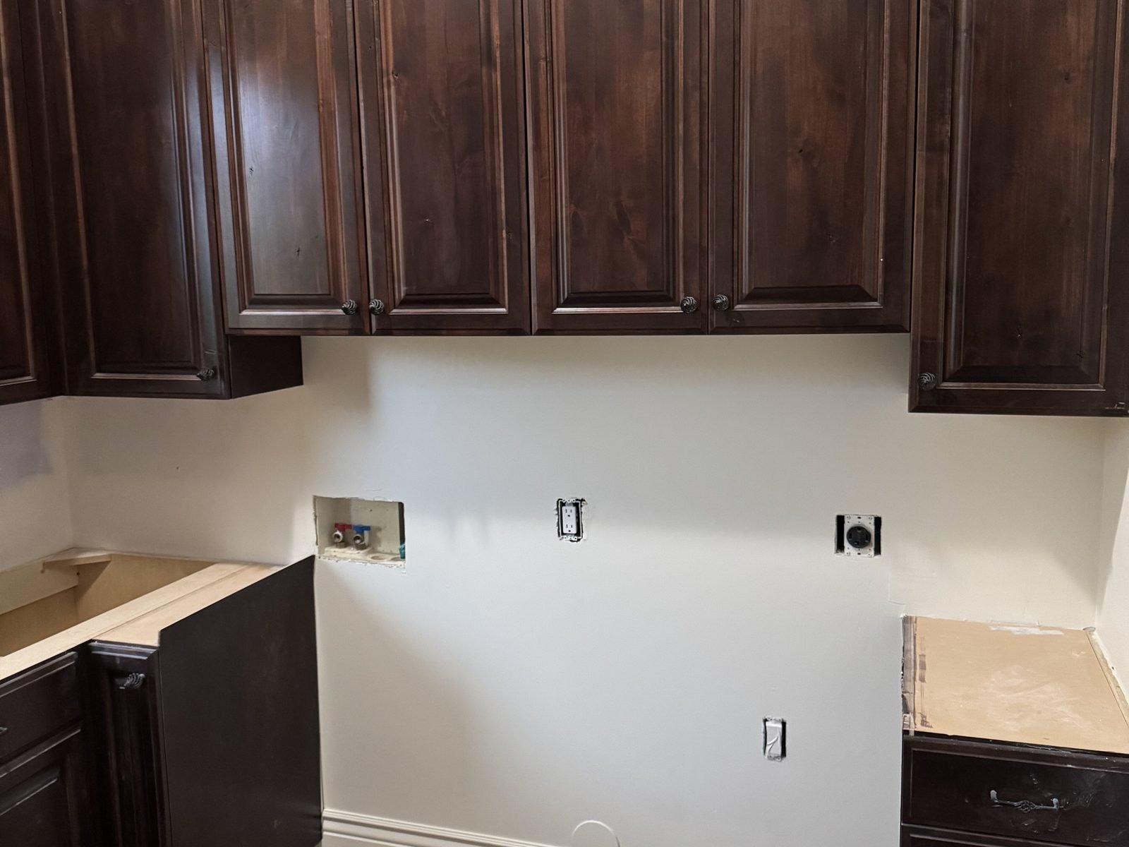 Dark-stained L-shaped upper cabinets in a laundry room before painting