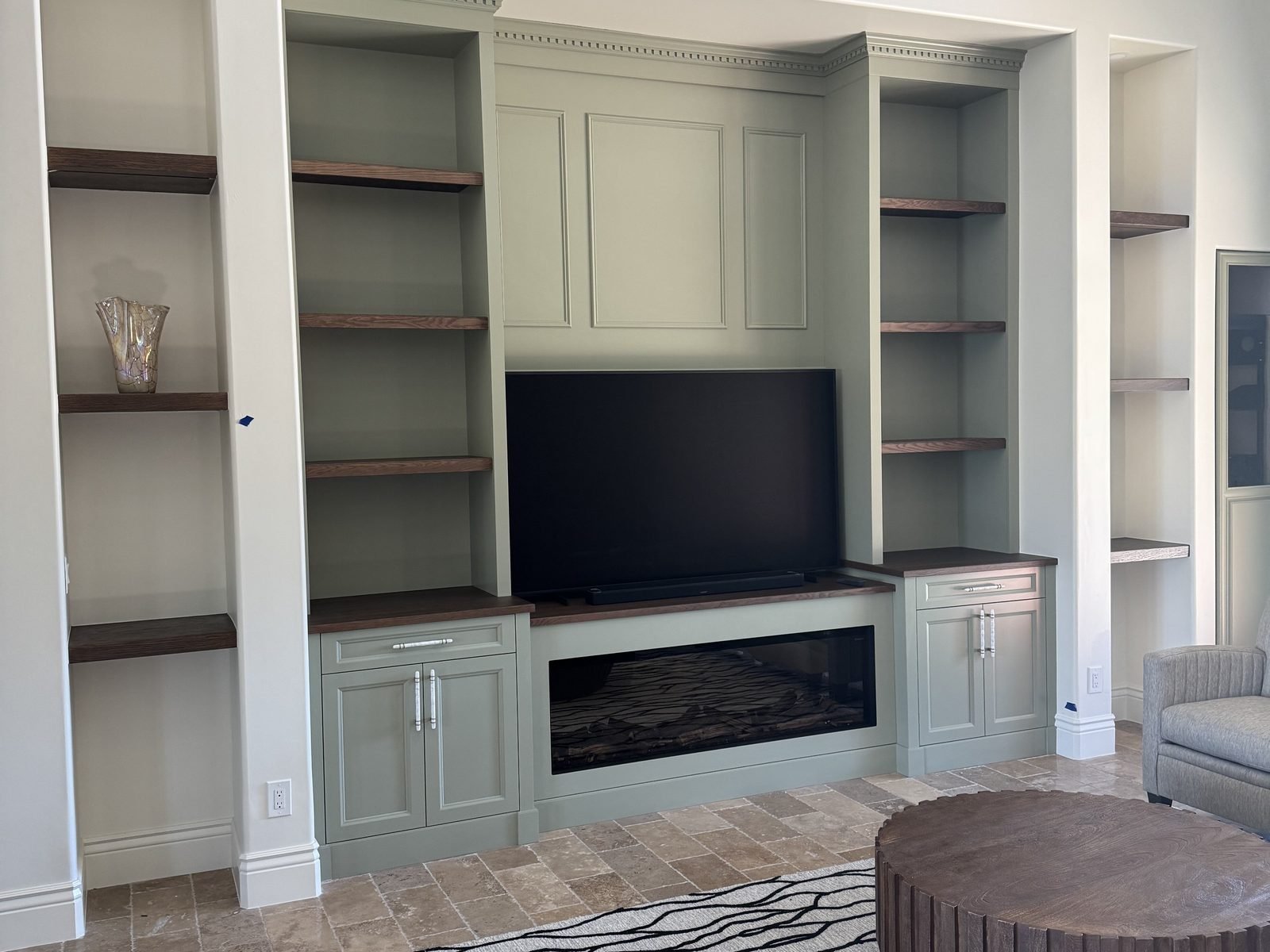 Finished built-in TV wall with sage green cabinetry, open shelving and a linear fireplace